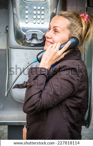 Girl in coat talking on the phone in a street telephone booth