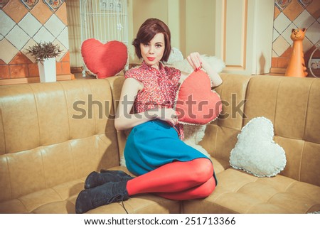 Young girl in red stockings sits on a couch and holding a big red heart