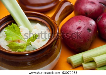 The crock of potato soup with celery spoon, accompanied by potatoes and celery sticks