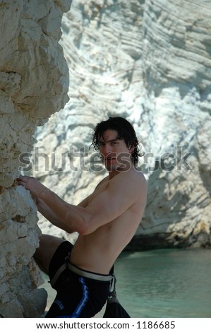 Young attractive shirtless male rock climbs the cliffs on an Adriatic beach in Southern Italy