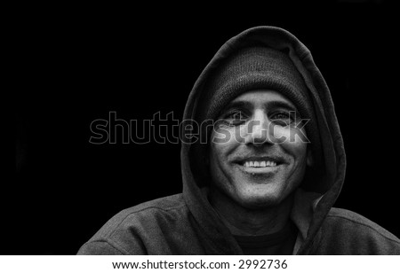 black and white portrait of a urban man wearing jacket with hood smiling on black background