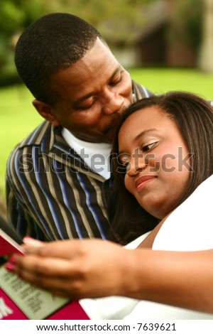 african american man kissing his wife who reading a book. focus on the woman