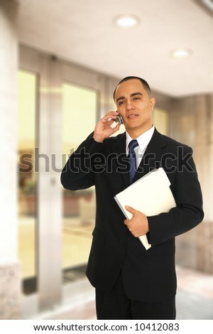 business man holding folder and making a phone call to his coworker in front of his office main entrance
