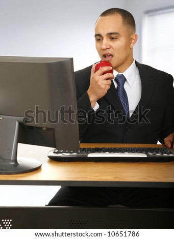 a man eating snack or apple while working in front of his computer in modern office space