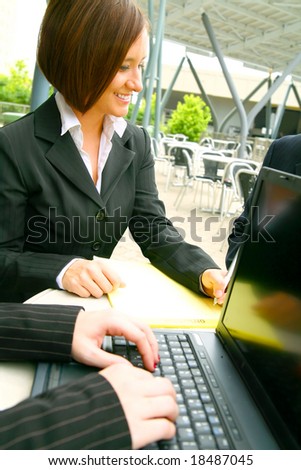 show of smiling business woman writing with hand of other woman typing on laptop on foreground