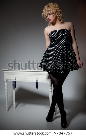Beautiful female in polka dot dress posing next to dressing table