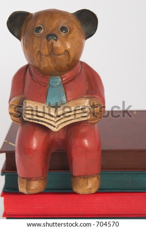 carved wooden bear reading a book sitting on pile of books