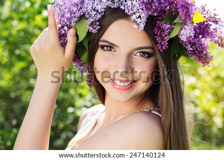 Close up portrait of beautiful smiling girl with fashion makeup is wearing beautiful wreath of lilac flowers