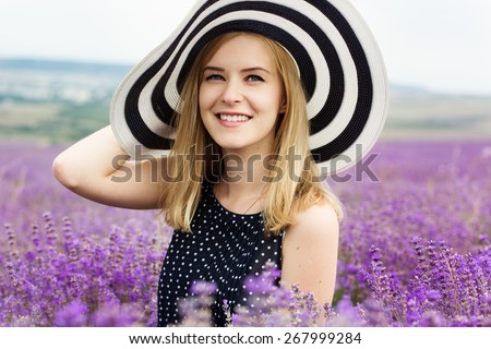 Beautiful blonde smiling girl is wearing stripped hat in fairy field of lavender. Summer time