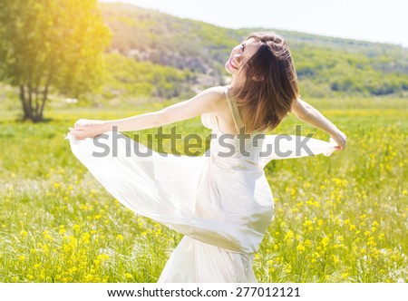 Beautiful girl in the field of yellow flowers is wearing flying white wedding dress