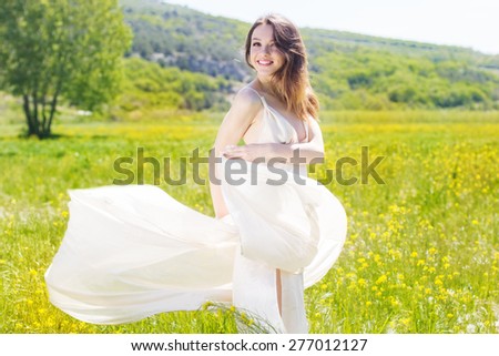 Beautiful girl in the field of yellow flowers is wearing flying white wedding dress