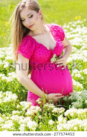 Happy pregnant woman is wearing pink dress on nature, pregnancy girl