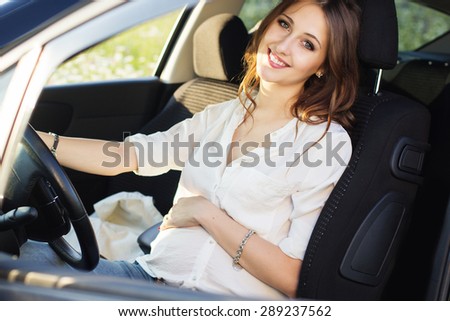 Pregnant smiling pretty woman in sitting at the wheel in car, sunset time