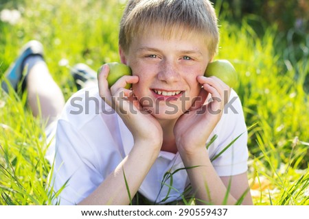Portrait of cute smiling boy with freckles on his face is holding two green apples