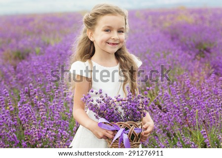 Pretty cute child girl is resting in a lavender field holding a basket full of purple flowers