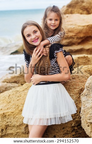 Two pretty smiling friends girls are wearing dresses sitting on the beach, summer time