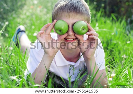 Portrait of cute smiling boy with freckles on his face is lying on green grass with green apples