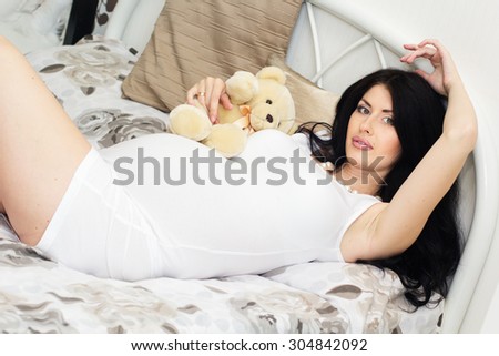Beautiful pregnant woman is lying on bed with teddy bear