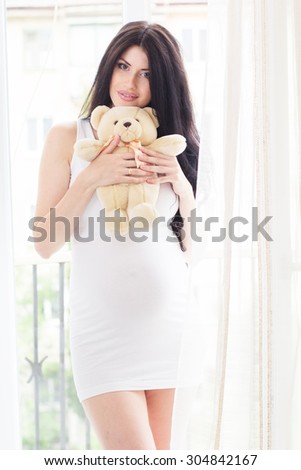 Beautiful pregnant woman is holding and hugging toy teddy bear