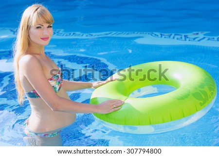 Beautiful smiling pregnant woman is holding green rubber ring in swimming pool, water aerobics