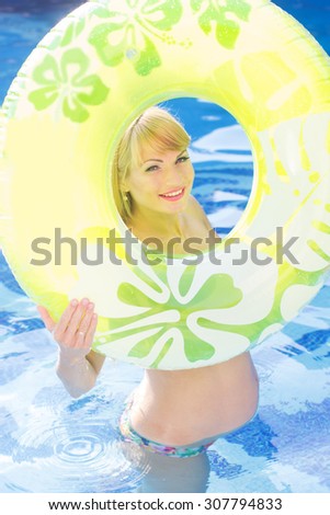 Beautiful smiling happy pregnant woman is holding green rubber ring in swimming pool, water aerobics