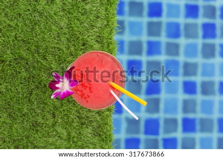Frozen margarita with strawberry on grass near swimming pool