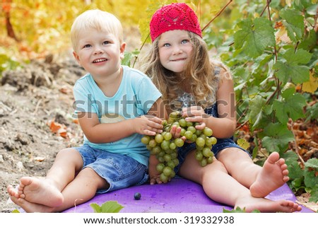 A cute two happy childrens friends outdoor are holding bunch of grapes in autumn vineyard