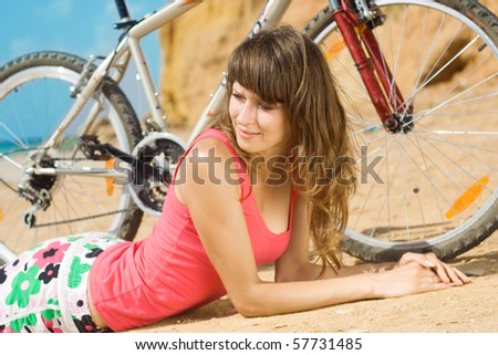 The beautiful girl has a rest on a beach with a bicycle