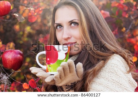 portrait of beautiful girl in autumn leaves. With an cup in hand.