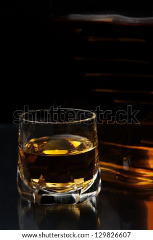 a glass and a bottle of hard liquor against black background