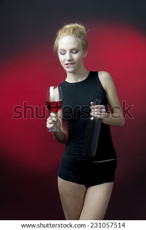 beauty blond model holding wineglass with red wine and wine bottle biting her lower lip