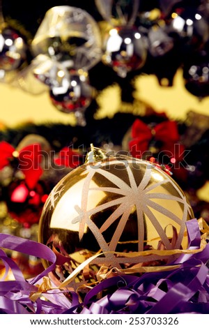 gold shiny Christmas ornament, placed on violet ribbon,Christmas tree at the background