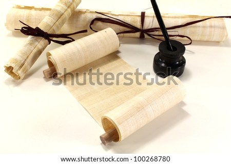 yellowed papyrus scrolls with quill and inkwell on a light background