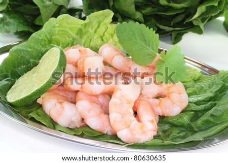 fresh shrimp with lime, lemon balm and lettuce on a silver platter before white background