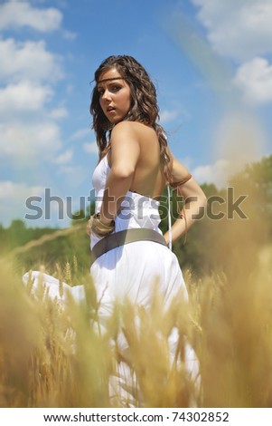 Beautiful woman standing in the middle of a golden wheat field on a hot summer afternoon. Color image with warm tones and a fresh feeling good for lifestyle and healthy themes.