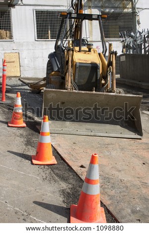 An urban construction zone with a front loader tractor, orange cones and steel plates.