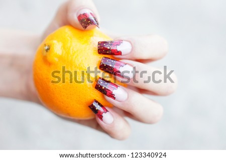 Beautiful female hand with unique curtain nail art design holding an orange