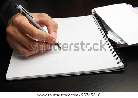Male hand writing on a notepad, stack of mail in the background.