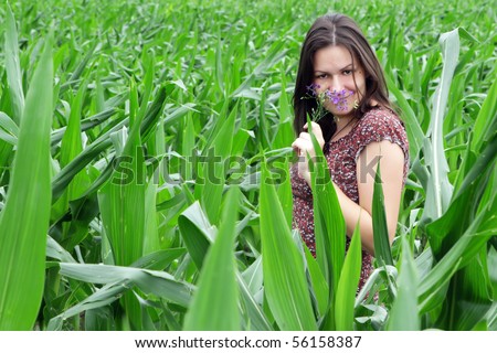 Beautiful girl in corn field smelling purple flower