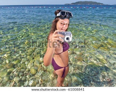 Young woman with diving mask taking picture of you on the beach with her waterproof camera