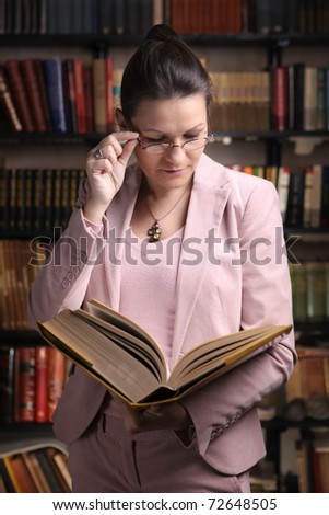 Female reading a thick old book in front of colorful bookshelf