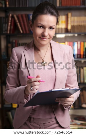 Attractive business woman in pink suit holding clipboard and pink  highlighter in library