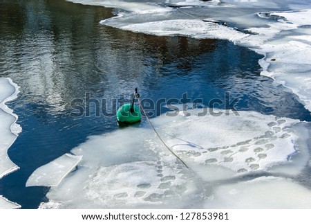 Hole in the ice with  ice flakes and a green buoy.