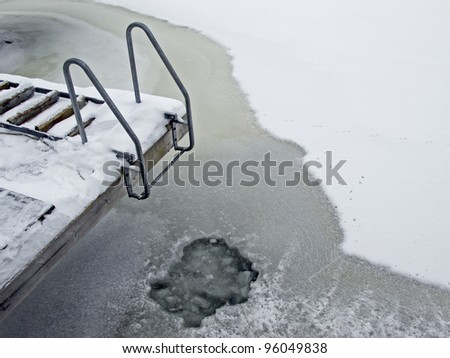Bridge with ladder in winter with frozen sea and an open hole in the ice.