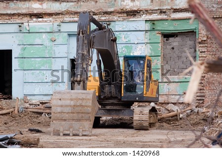 Yellow caterpillar excavator during building demolition, green wall on background