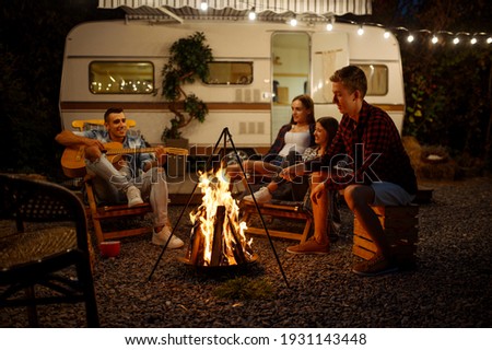 Friends playing on guitar by the campfire, camping
