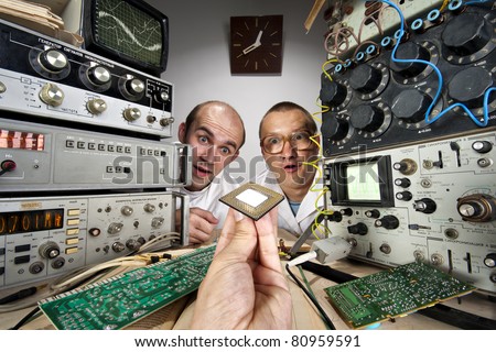 Two funny nerd scientists at vintage technological laboratory looking at modern computer processor