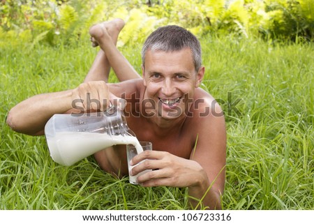 The happy adult man drinks fresh milk upon green grass