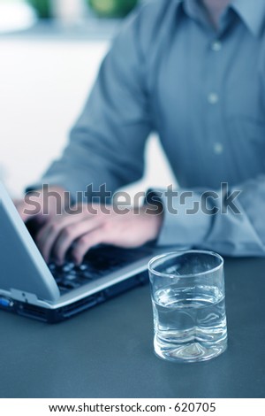 Business man writing on his laptop with a glass of water near