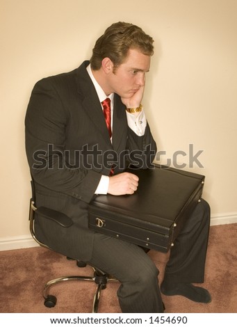 Business man in black suit, white shirt, and red tie holding his briefcase in a confused, tired expression